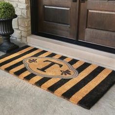 a black and yellow door mat with the letter t on it next to a potted plant