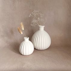 two white vases with dried flowers in them on a beige background, one is empty