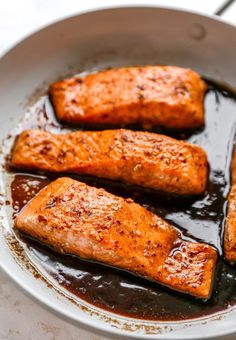 four pieces of cooked salmon are in a skillet with brown sauce on the side