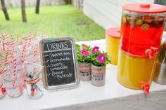 a table topped with drinks next to a chalkboard sign and potted plants on top of it