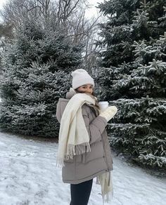 a woman is standing in the snow with her scarf around her neck and hat on