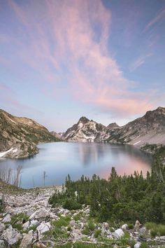 a lake surrounded by mountains and trees under a blue sky with clouds in the distance