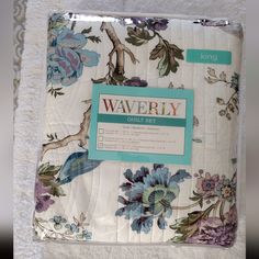 a white blanket with blue and purple flowers on it, next to a bed sheet