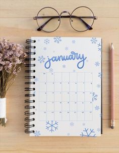 a calendar with the word january written on it next to a pen, glasses and flowers