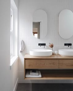 two white sinks sitting on top of a wooden counter in a bathroom next to mirrors