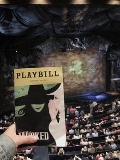 a person holding up a playbill book in front of an auditorium full of people