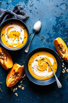 two bowls filled with soup next to spoons on a blue tablecloth and napkin