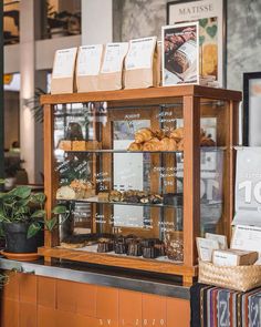 a display case filled with lots of pastries on top of a wooden counter next to a potted plant