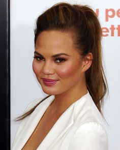 a close up of a person wearing a white suit and smiling at the camera with her hair in a ponytail