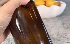 a hand holding a bottle of wine in front of a bowl of oranges and lemons