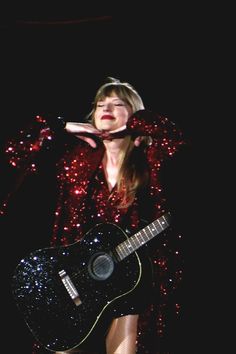 a woman in red is holding a black guitar