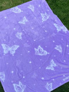 a purple blanket with white butterflies on it sitting in the grass next to a teddy bear