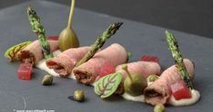 several small appetizers are arranged on a gray surface, including asparagus and prosciutto