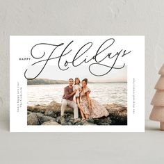 a holiday card with an image of two people sitting on rocks next to the water