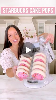 a woman is holding up some pink donuts