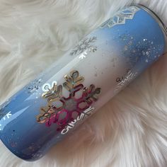 a blue and white cup with snowflakes on it sitting on a fur covered surface