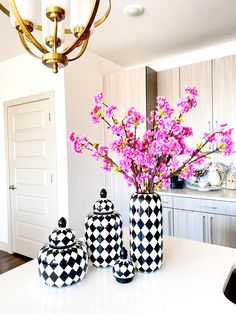 three black and white vases with pink flowers in them sitting on a kitchen counter