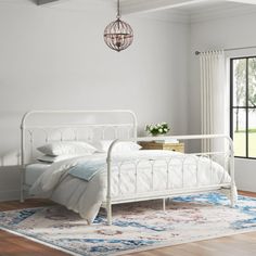 a white bed sitting in a bedroom on top of a hard wood floor next to a window