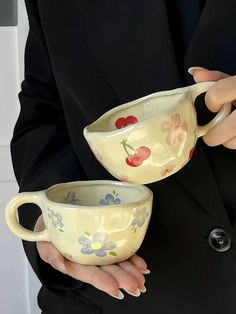 the woman is holding two cups with cherries painted on them, both in their hands