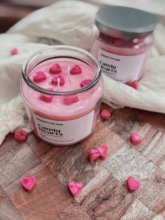 two jars filled with pink hearts sitting on top of a wooden table next to a white towel