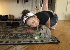 a woman laying on the floor next to a cat with a drink in it's mouth