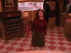 a woman in a red sweater and plaid skirt standing in a room with checkered floor