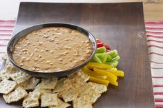 a plate with crackers, peppers and cheese on it next to a bowl of dip