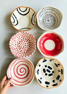 four bowls with different designs on them and one being held up in the air by someone's hand