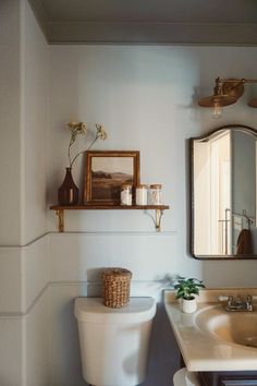 a white toilet sitting next to a bathroom sink under a mirror on top of a wall