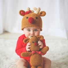 a baby is sitting on the floor holding a teddy bear and wearing a crocheted hat