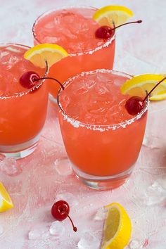 three glasses filled with watermelon lemonade and cherries next to sliced lemons