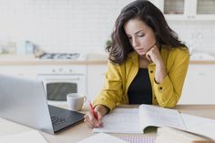 a woman sitting at a table in front of a laptop computer and holding a pen