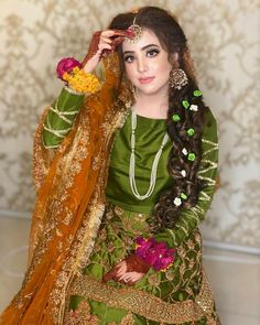 a woman in a green and gold dress with flowers on her head, holding a yellow shawl