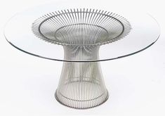 a glass and metal table with a circular base on the top, in front of a white background