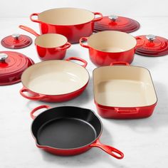 red pots and pans are arranged on a white countertop, with one black frying pan in the middle