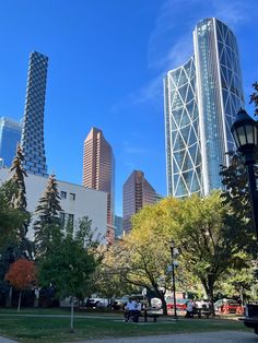 a park with benches and trees in the foreground, skyscrapers in the background