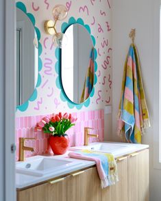 a pink and blue bathroom with flowers on the sink, mirror and towels hanging in front of it