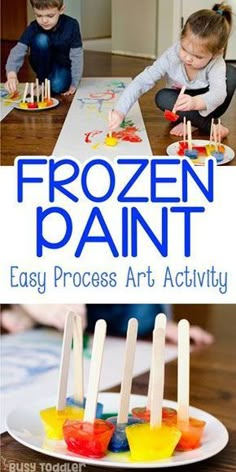 two children playing with frozen paint and pops sticks on a table in front of them