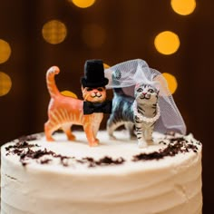 two cats are standing on top of a wedding cake with the cat figurine next to them