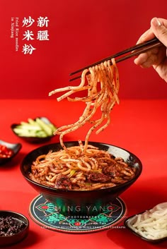 a person holding chopsticks above a bowl of noodles with sauce on the side