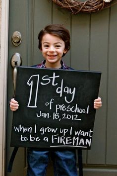 a young boy holding up a sign that says, 1st day of preschool june 15, 2012 when i grow up i want to be a fireman