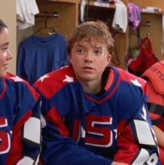 two young men sitting next to each other in a dressing room with sports gear on the walls