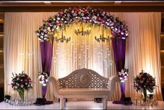 a white couch sitting under a purple and white flower covered arch on top of a stage