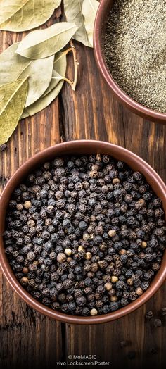 two bowls filled with spices on top of a wooden table next to leaves and pepper