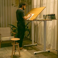 a man writing on a piece of paper in front of a table with stools