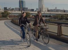 two people riding bikes on a bridge in the city