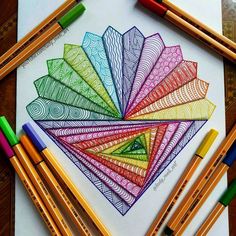 colored pencils and crayons are sitting next to a drawing with an intricate design on it