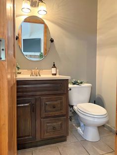 a white toilet sitting next to a wooden sink vanity in a bathroom under a round mirror