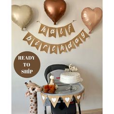 a table with a cake and some balloons on the wall behind it that says happy birthday ready to ship