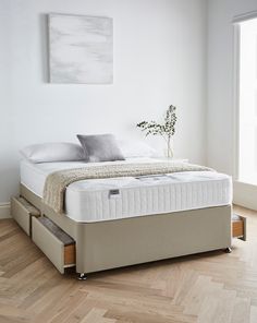 a bed with two drawers underneath it in a white room next to a wooden floor